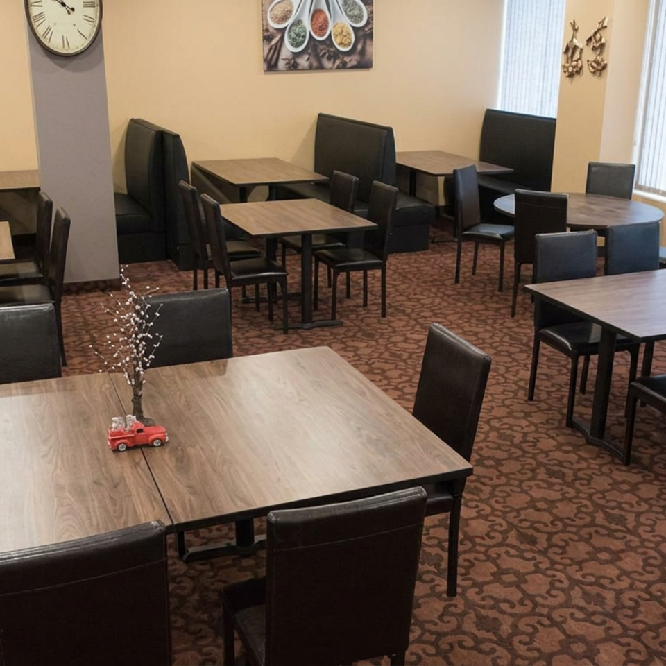 Spacious restaurant dining room with wooden tables, black chairs, patterned carpeting, wall art, and large windows.