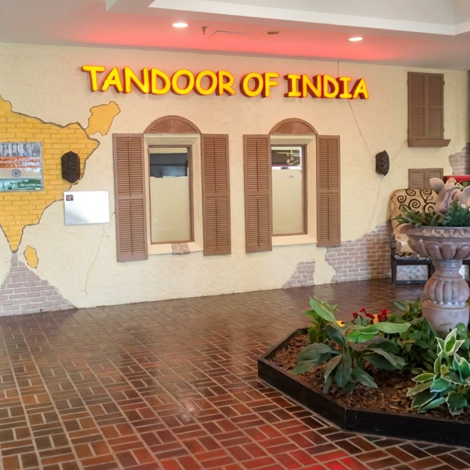 Tandoor of India restaurant entrance with an India map mural, shuttered windows, ornate planter, and indoor greenery.